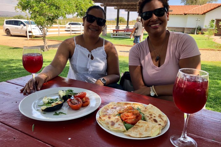 a person holding a plate of food on a picnic table